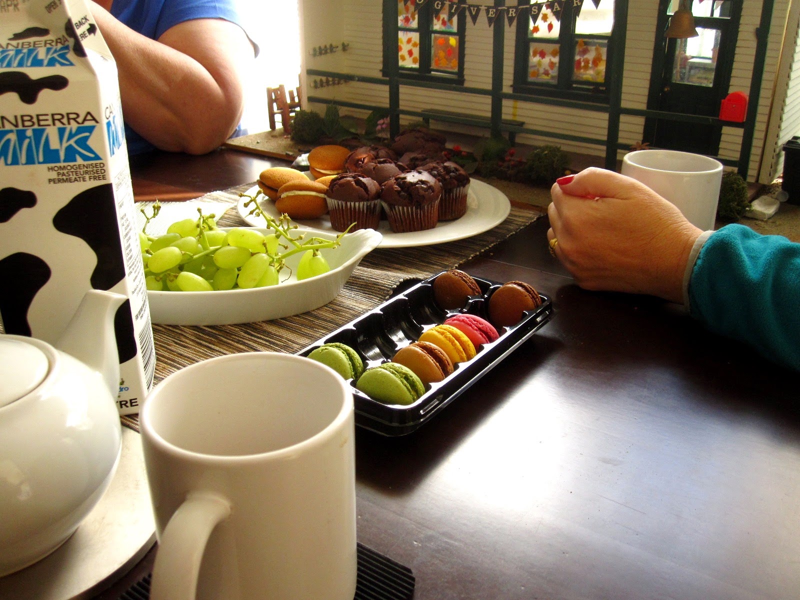 A selection of morning tea treats set out on a table in front of a modern miniatures dolls' house school
