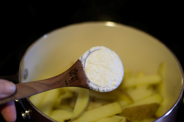 Flour being added to the potatoes in the pot. 
