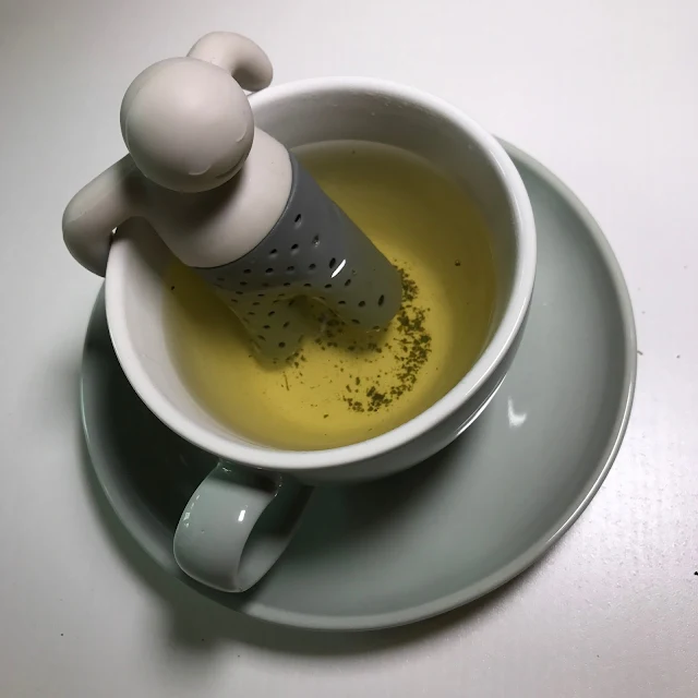 A tea infuser shaped like a man relaxing on the edge of the cup infusing tea into a plain tea cup and saucer