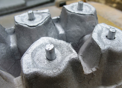 Four modern dolls' house miniature spray cans, poked into the bottom of an egg carton and  spray painted.