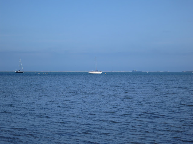 Very blue sea and sky with two sailing boats moored against buoys.