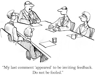 In a cartoon, the boss at the head of the board room table tells others not to be fooled by his "appearing" to be inviting feedback.