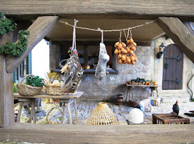 Medieval market hall with game and onions hung from the ceiling, and tables of produce under.