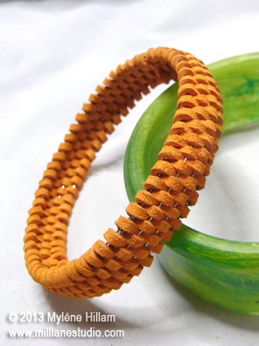 Domed suede lace bangle propped against a green resin bangle.