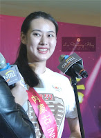 A female participant of the Miss Chinese World from Qing Dao smilling happily in front of a microphone