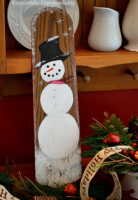 Painted snowman a ceiling fan blade on a table with Christmas Decor