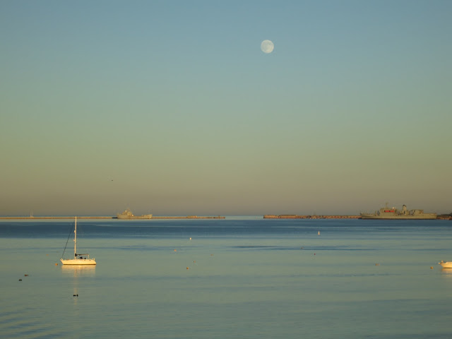 Tranquil water with yacht, frigate and harbour wall.