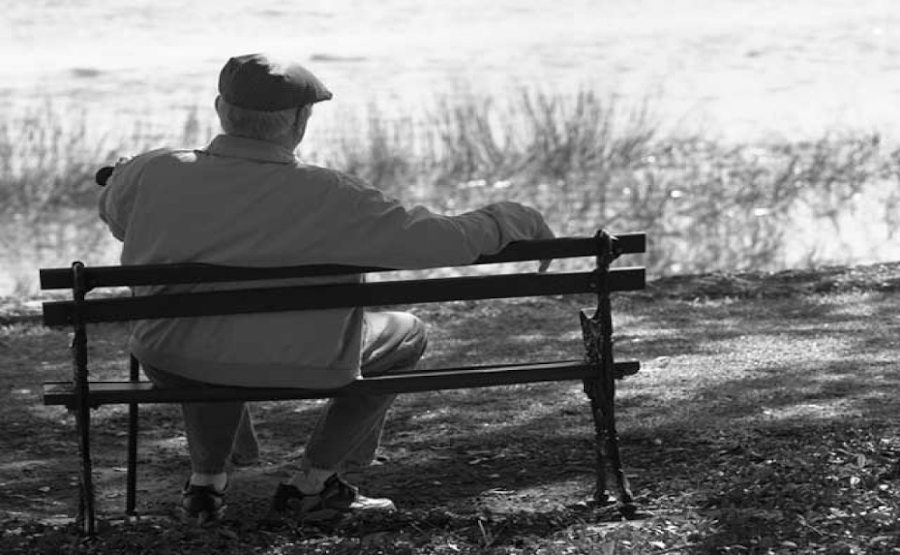 Anciano con alzheimer sentado en un banco de espaldas a la cámara, mirando al horizonte.
