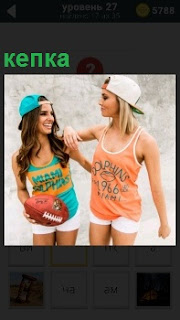 Две девушки в спортивной форме и кепке на голове держат мяч для игры в своих руках, одетые в шорты