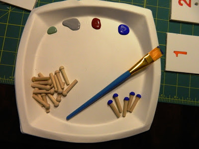 DIY Peg Board Game: Items for making some blue-painted pegs (paintbrush, paints, pegs).