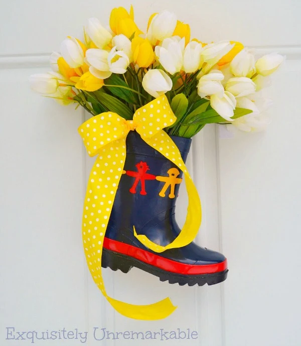 A Rubber Rain Boot Vase filled with tulips and a yellow ribbon on a front door