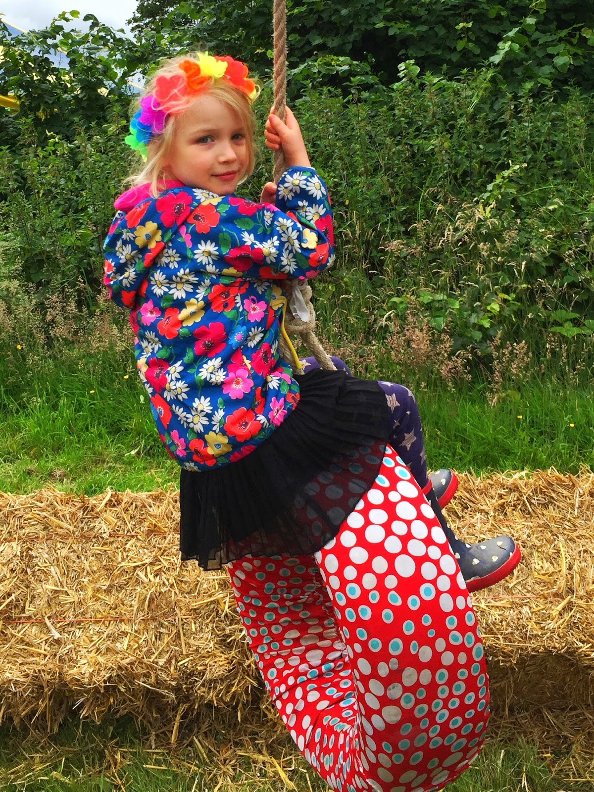 4 year old on a tyre swing in bright clothes and wellies. She has a flower garland on her head and is at 3 foot people festival in Chelmsford 2016