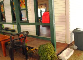 Entry to a miniature dolls' house school with garden chair and a table outside.