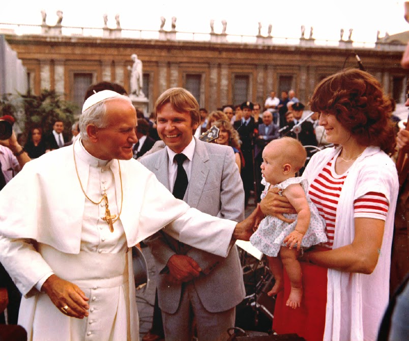Aug. 13, 1980, Living Sound Vatican concert and audience with Pope John Paul II. Pictured L/R Pope John Paul II, Mike McKibben (behind His Holiness), Joel Vesanen (Team III Road Manager), Nancy McKibben, Baby Carrie McKibben (four months old), Nancy McKibben, Living Sound III (in background). This photo was captured at the foot of the steps of St. Peter’s Bascilica