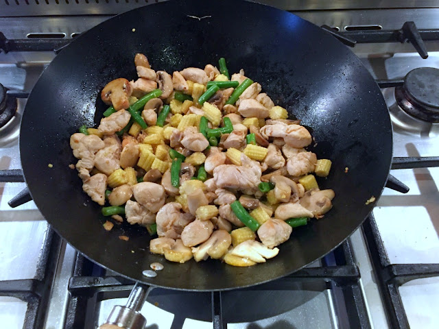 chicken, corn, mushrooms, green beans frying in a black wok