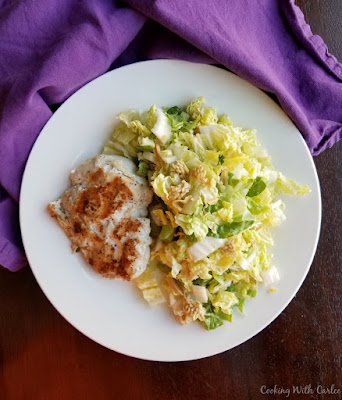 dinner plate with napa salad on one side and a chicken breast on the other