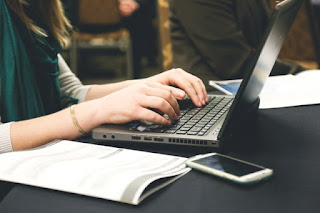 Writing the Plot A woman writes on a laptop upon a black desk