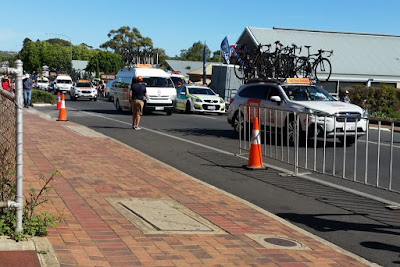 A view from the paved footpath of Main Road McLaren Vale as the team cars and buses arrive. Portable fencing and orange traffic cones can be seen.