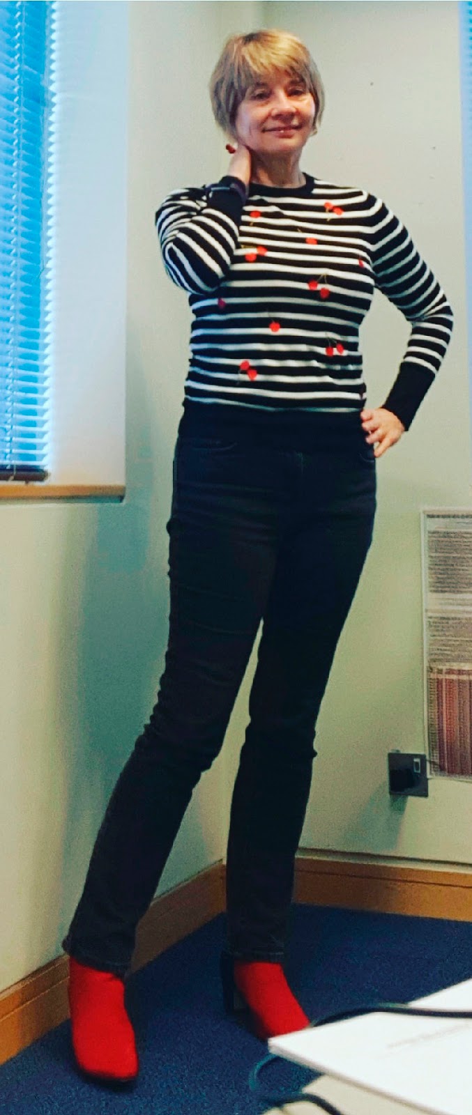 Image showing an over 40s woman in casual work outfit of black jeans, black and white striped jumper with cherries and red boots