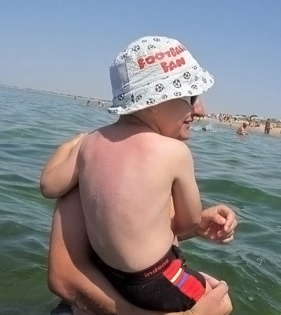 Denizdeyken yüzü, kucağında olduğu babasının yüzüyle birleşerek karışmış olan bir çocuk gösteren göz yanılması resmi
