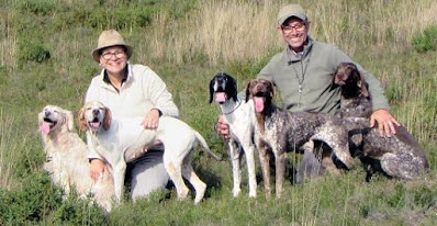 Casal agachado em um campo a segurar 5 cães