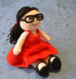 Kwokkie Doll seated and wearing her red sundress, black sandals and black spectacles.