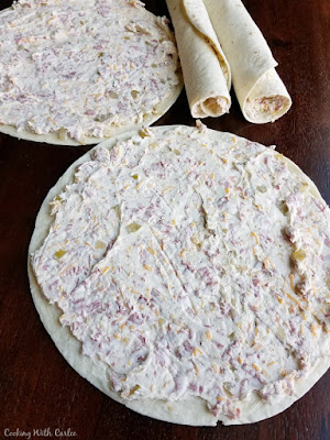 cream cheese and beef mixture spread out over large tortilla with some rolled tortillas in the back