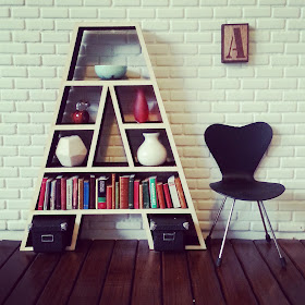 Modern doll's house bookcase in the shape of a letter A, filled with books and ornaments.