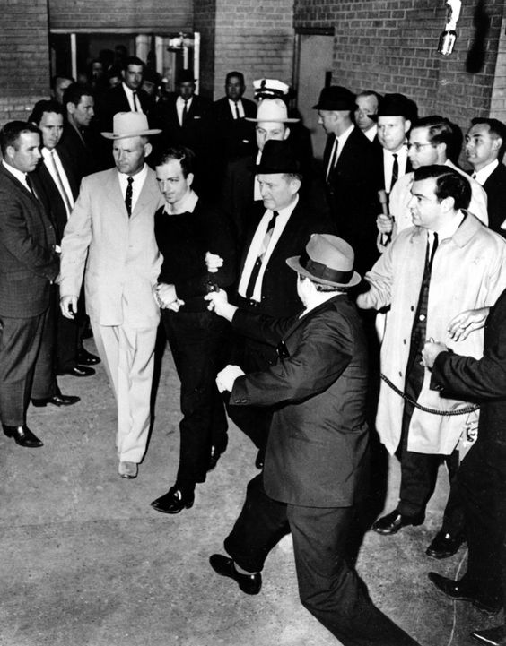 On November 24, 1963, two days after Kennedy's assassination, suspect Lee Harvey Oswald is escorted to the Dallas city jail as Dallas nightclub owner Jack Ruby approaches with gun drawn. Bypassing a cordon of police officers, Ruby shot Oswald in the abdomen, an act inadvertently captured on live television by reporters filming the prisoner transfer. Ruby was convicted of Oswald's murder and spent his remaining days in prison.