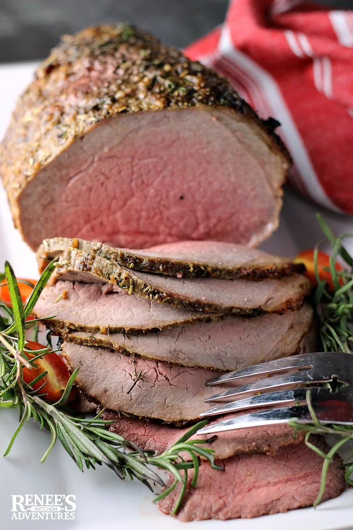 Eye of Round Roast on white platter sliced with fresh rosemary and grape tomatoes