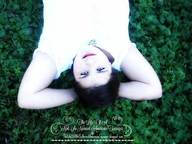 What does God Sound Like? Young woman lying on the ground in the grass looking up at the sky peacefully wearing a white skirt and shirt and she has blue eyes and brown hair.