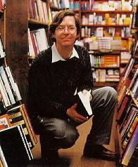 Man kneeling holding book amid shelves of books.