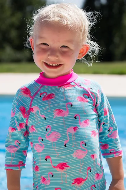 A grinning toddler in a long sleeve SPF sun suit