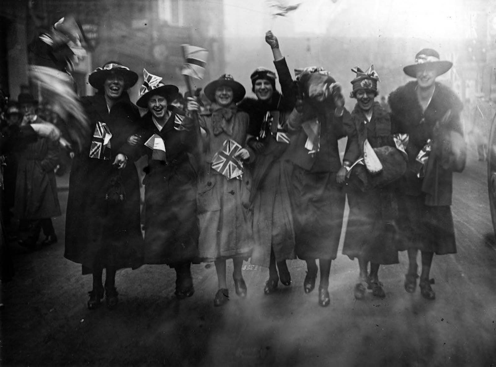 A group of women joyfully waving Union Jacks on Armistice Day.