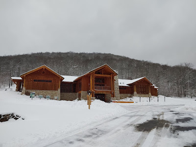 Wood and stone museum building with snow on the ground and wooded hillside in the background