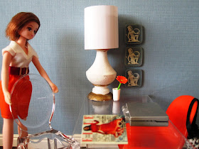 One-twelfth scale modern miniature office scene in shades of light blue and orange, with a dolls pulling out a visitors' chair on one side of the desk.