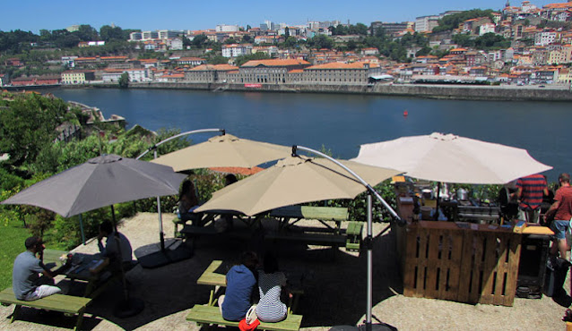 Pessoas sentadas em mesas com guarda-sol com vista para o rio Douro e para a cidade do Porto