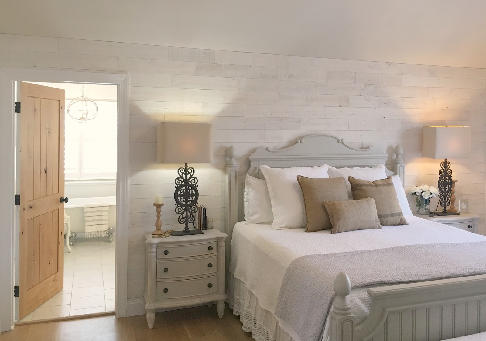 Serene European inspired country bedroom. Master bedroom with stikwood wood plank wall and knotty alder door to bathroom in Hello Lovely Studio fixer upper