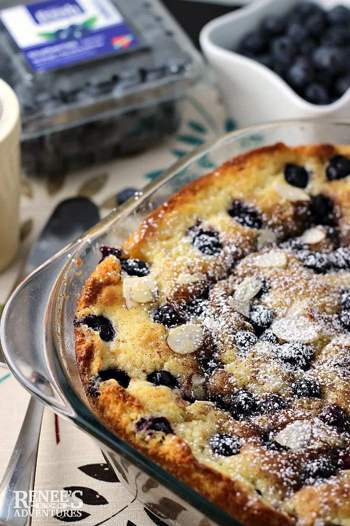 Blueberry Coffee Cake in pan in foreground and blueberry container with blueberries in background