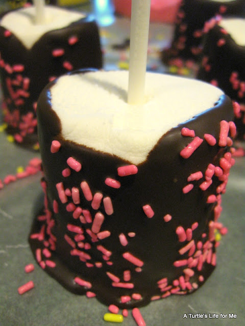 A photograph  of a marshmallow pop dipped in chocolate and covered with pink sprinkles