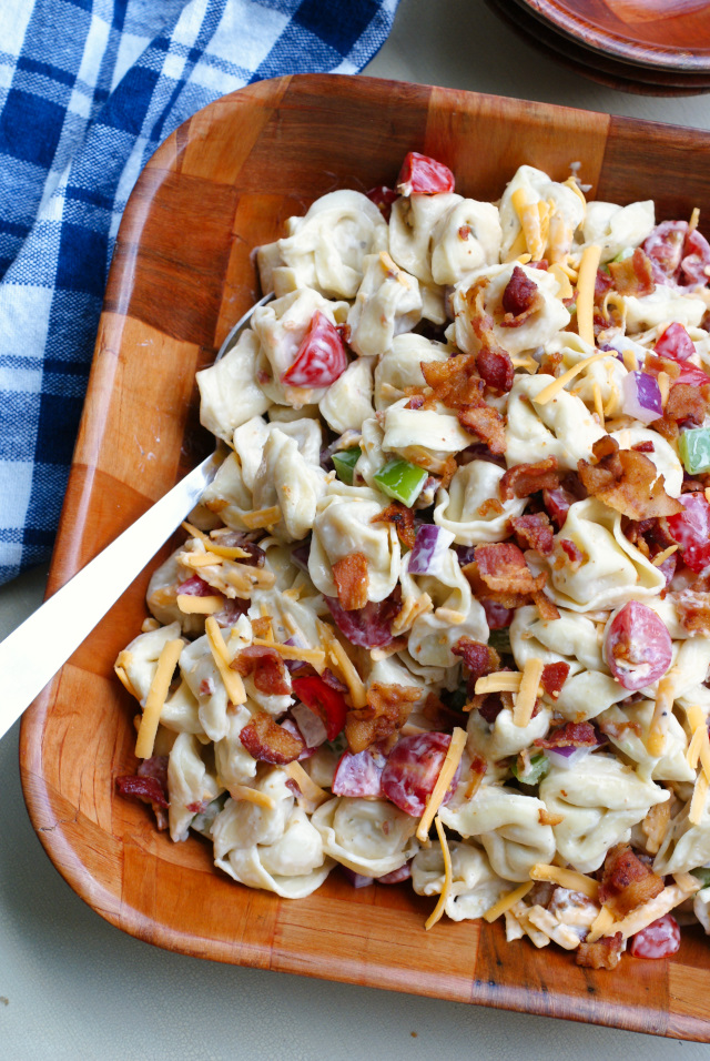 Bacon Ranch Tortellini Salad in a wooden bowl with a blue checkered kitchen towel next to it.