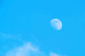 moon in blue sky with passing white clouds