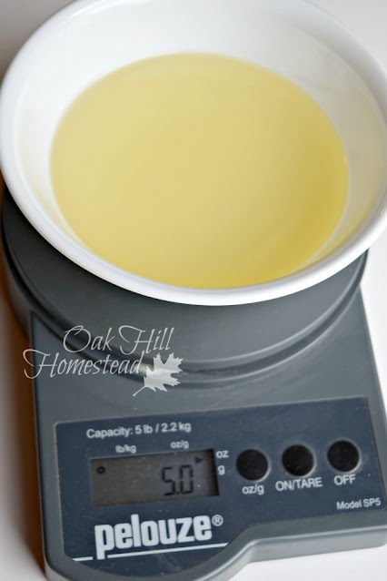 A white bowl with soapmaking oils on a digital scale.