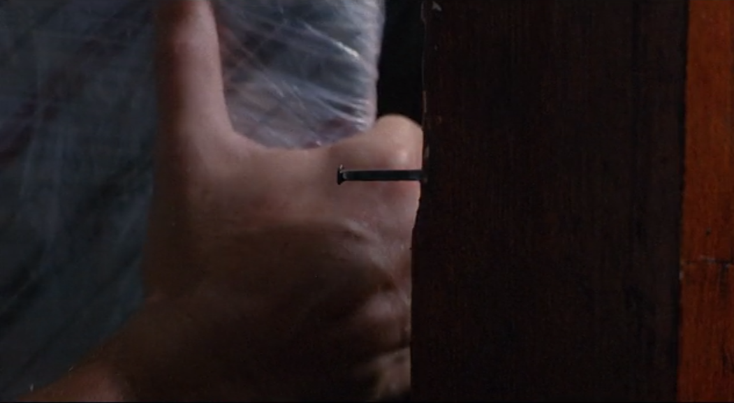 Larry carries a mattress up the stairs, a nail is uncomfortably close to his bare hand