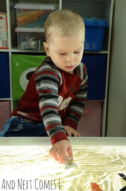 Toddler driving a moon rover figurine through moon dust on the light table
