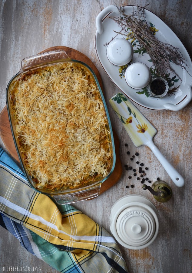 Vista cenital lasaña berenjenas en fuente de cristal sobre tabla de madera, bandeja porcelana con salero y pimentero, paño cocina de colores