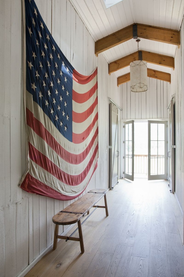 Everything Coastal Beach Cottage American Flag Decor A Large American Flag In White Washed Cottage Hallway With Wide Planked Floors And An Interesting Driftwood Like Bench Doors Thrown Open To The Sand