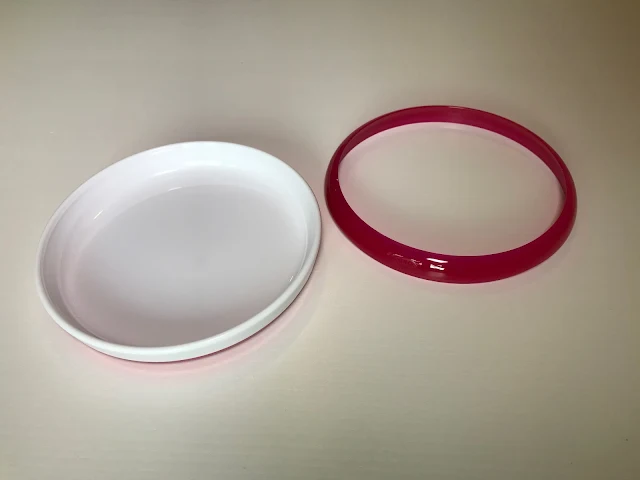 A white plastic circular plate next to a bright pink plastic ring which can attach to the top of the plate to provide a lip