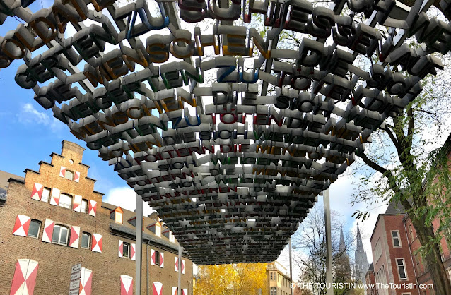 Art installation made from red, blue, yellow letters which honours deserters and war opponents from the time of National Socialism with a large cathedral in the distance.