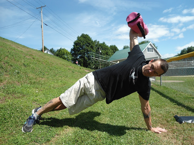 Man does side plank utilizing The Ultimate Sandbag in a grassy field